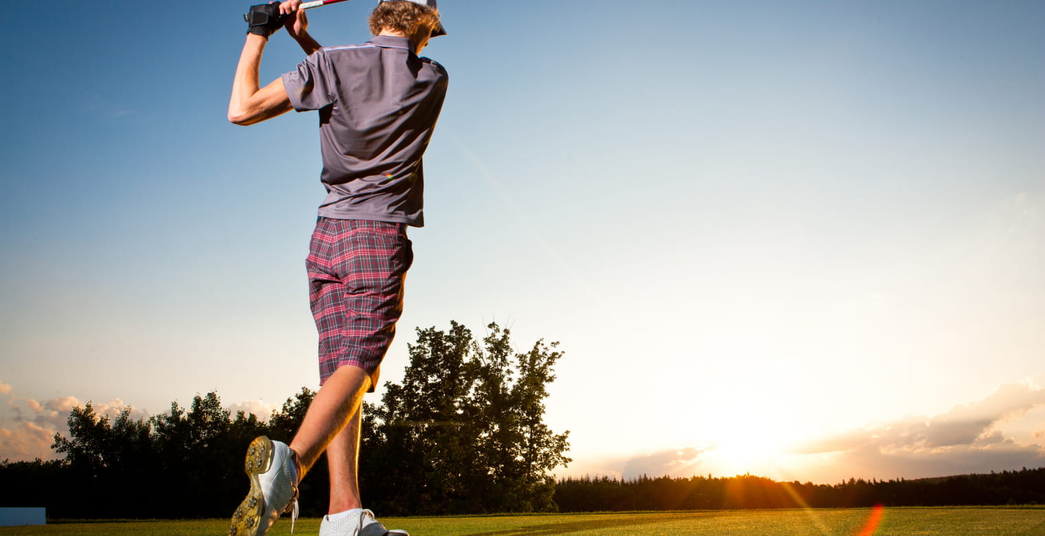 Male golf player teeing off golf ball from tee box to beautiful sunset